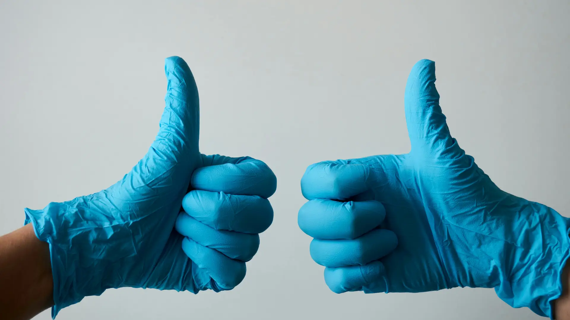 A medical professional holding up their thumbs up while wearing surgical gloves.