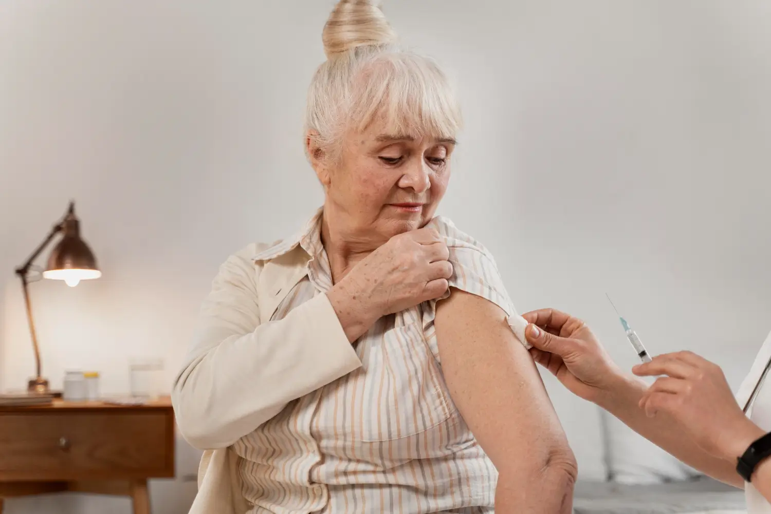A doctor preparing the injection site on the upper arm of an older woman.