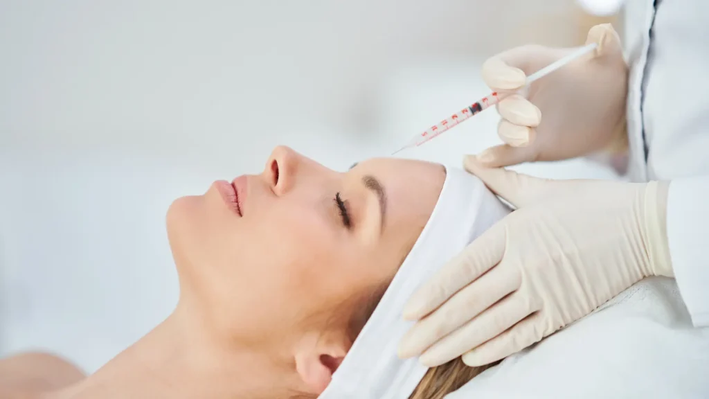 An individual administering a botox injection on their forehead.
