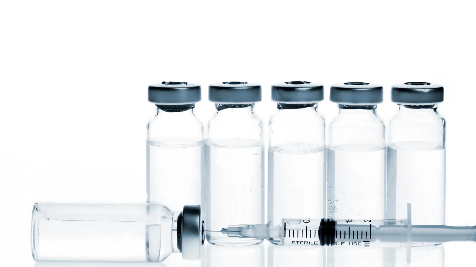 Numerous glass medicine vials lined up and a syringe.