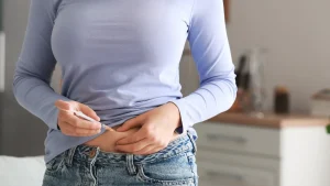An individual administering a self-injection on their abdomen, like Mounjaro therapy.
