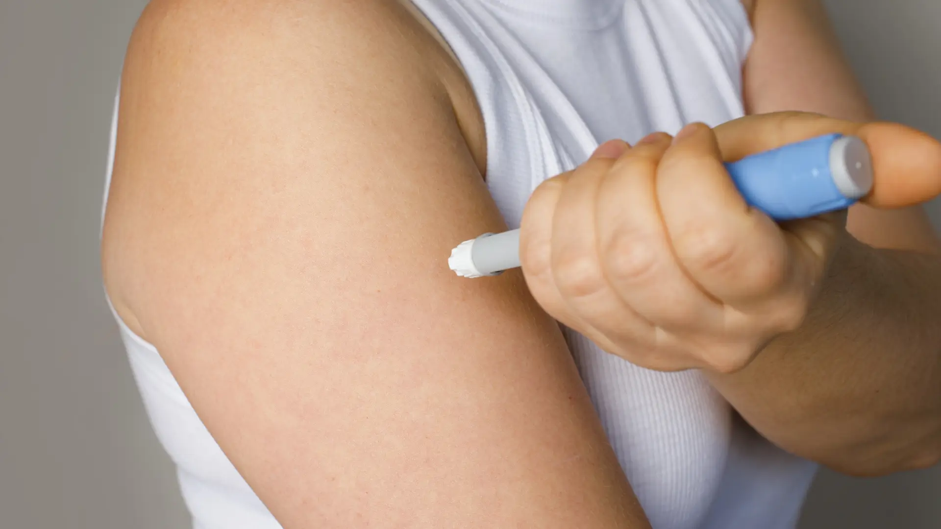 An individual administering a self-injection in their upper arm.