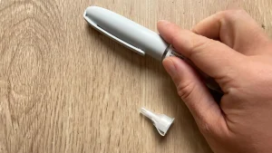 A hand holding tirzepatide (Mounjaro) injection pen with cap on a wooden surface.