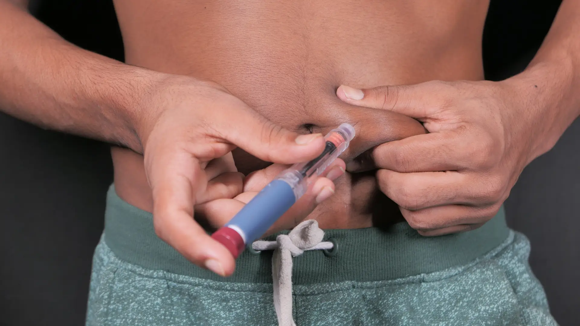 An individual administering an injection on their abdomen, like in administering on the proper Mounjaro injection sites.