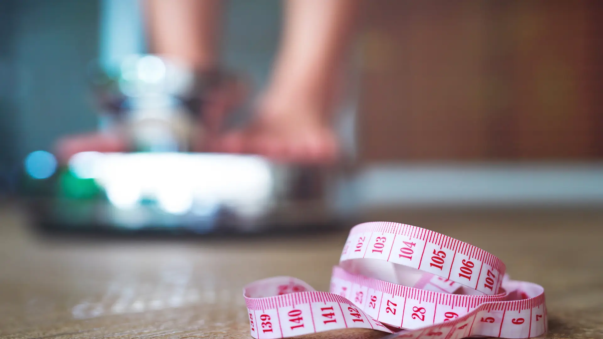 A close-up shot of a tape measure with an individual checking their weight as the background.
