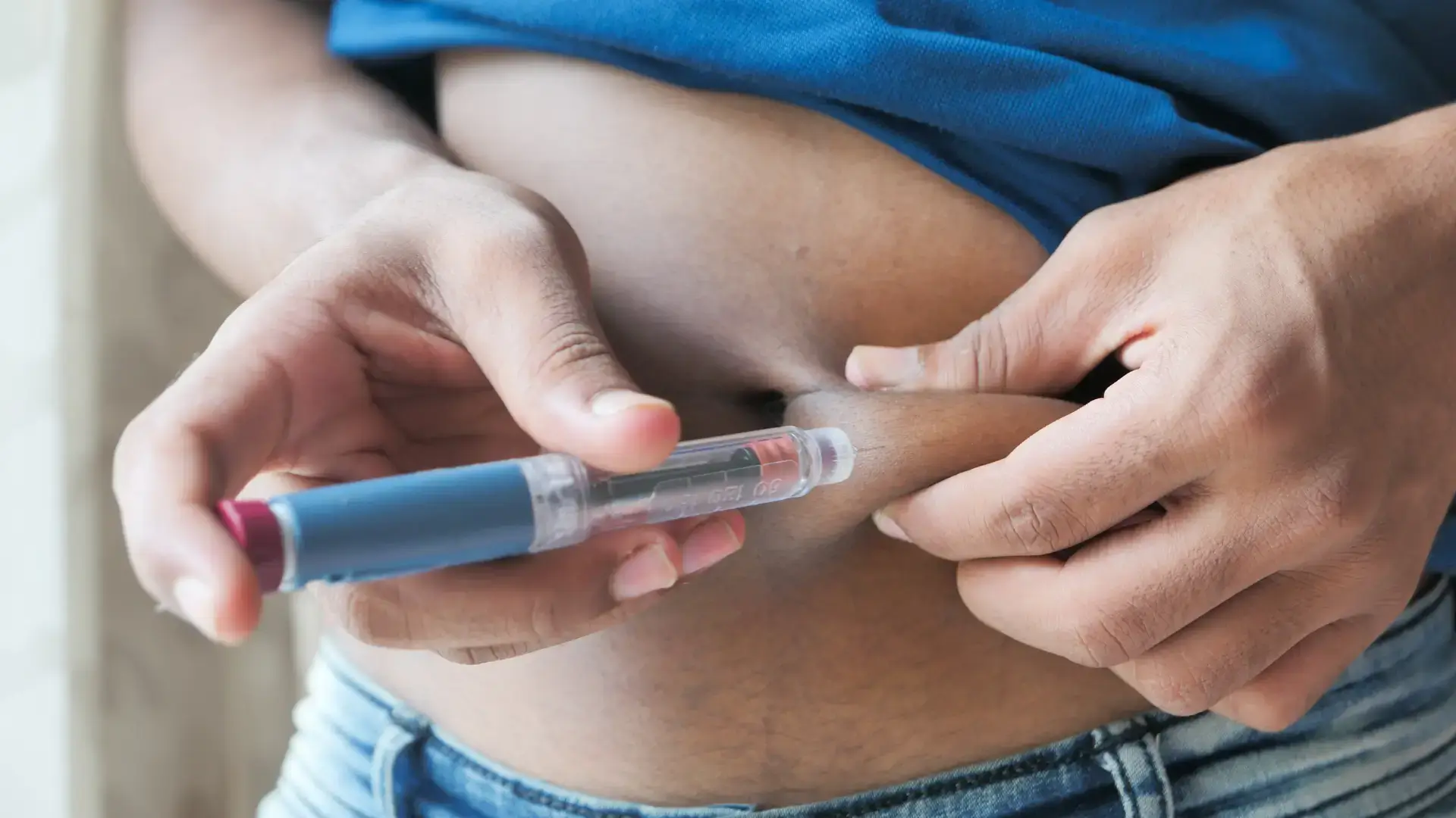 An individual self-injecting a medication treatment in their abdomen.