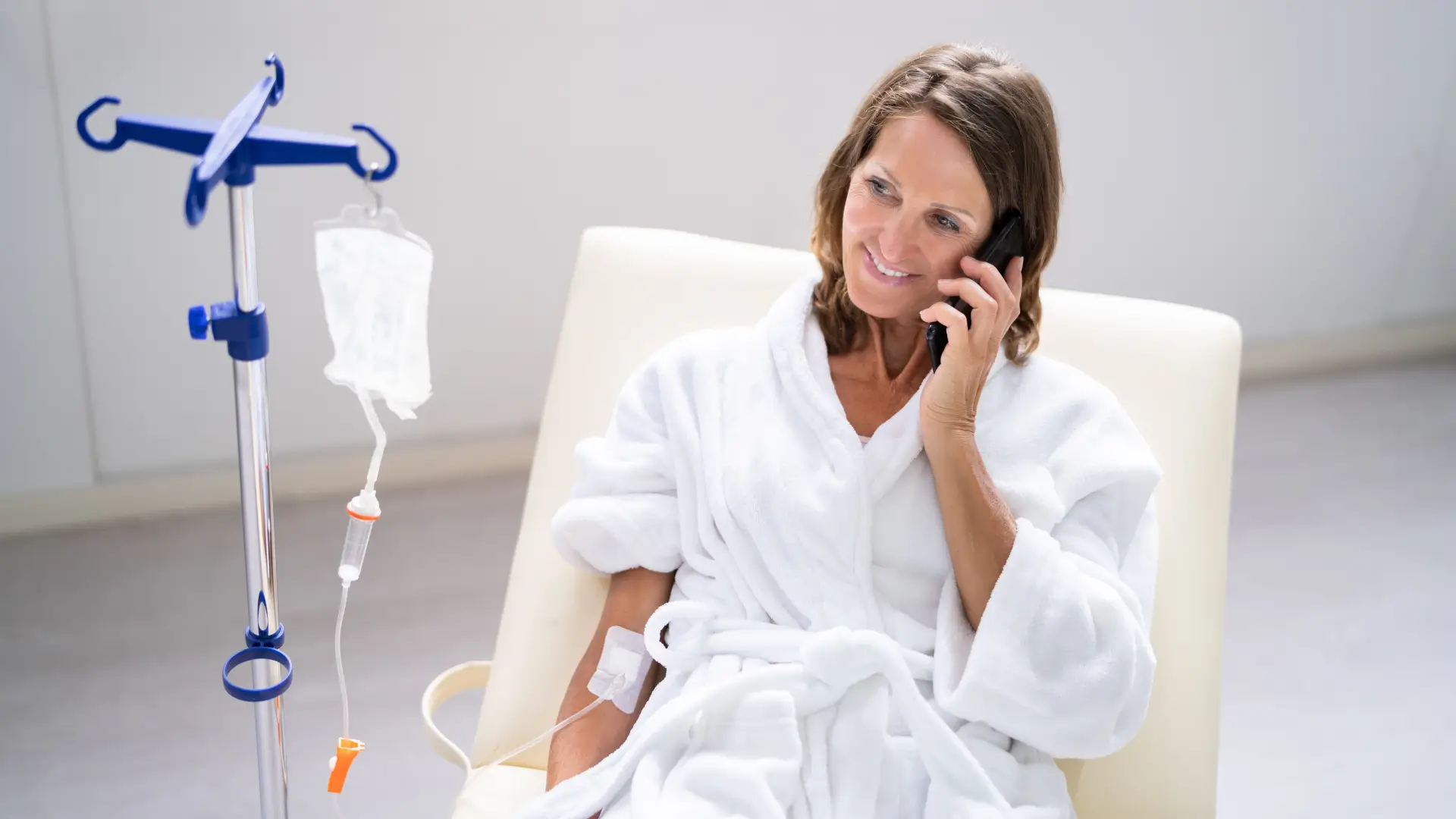 A patient undergoing an IV infusion like NAD IV therapy, while talking to someone on their smartphone.