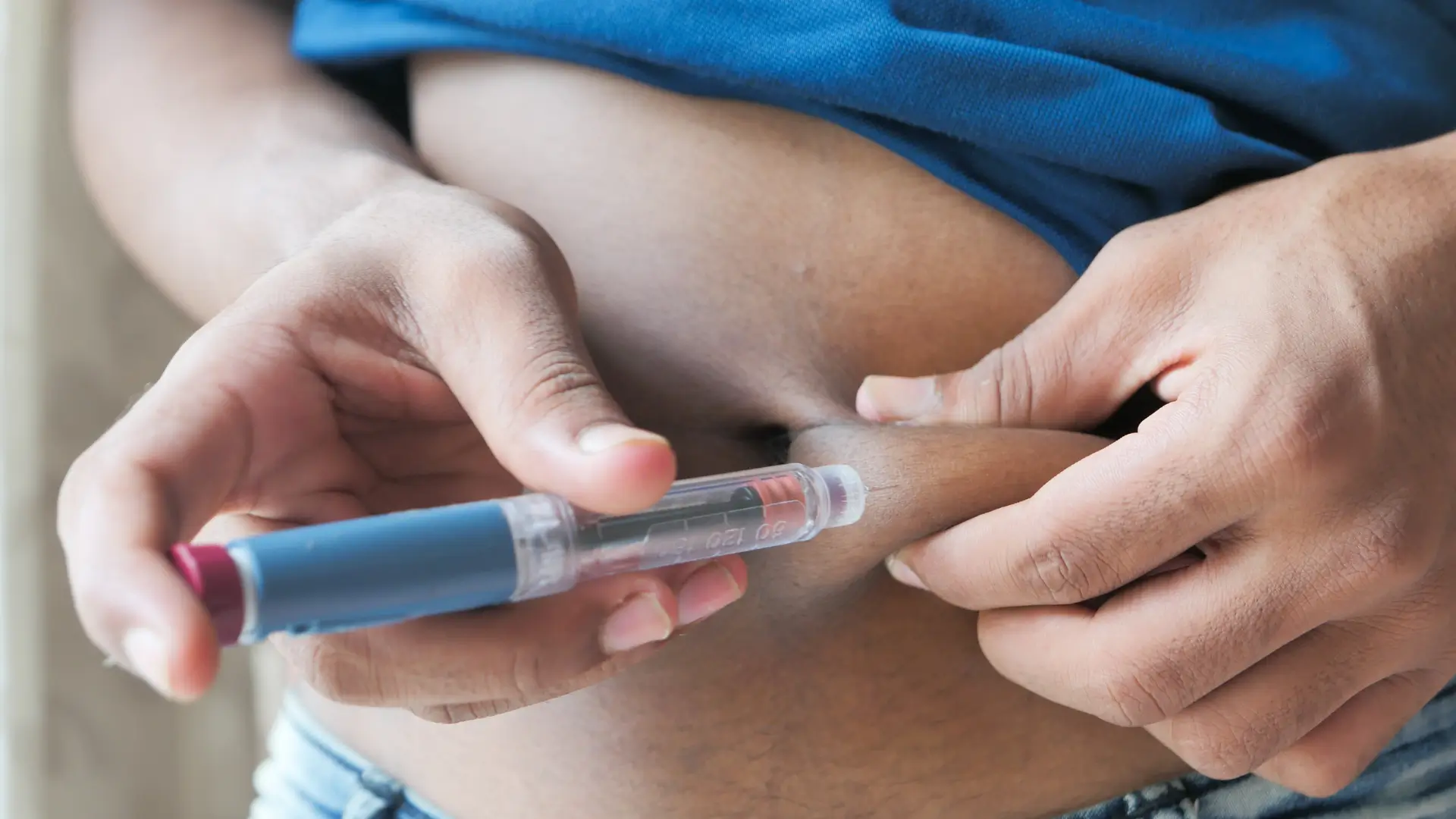 An individual using an injection pen on their abdomen.
