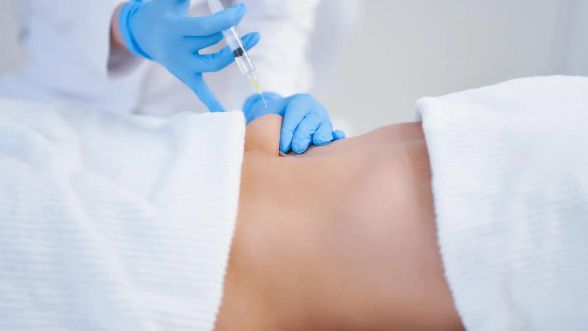 A medical professional administering an injection on the patient's abdomen, similar to how Xolair injection is administered.