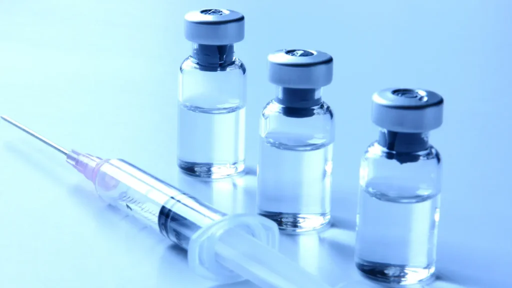 Three solution vials and an injection on a surface for research purposes, like retatrutide formulations.